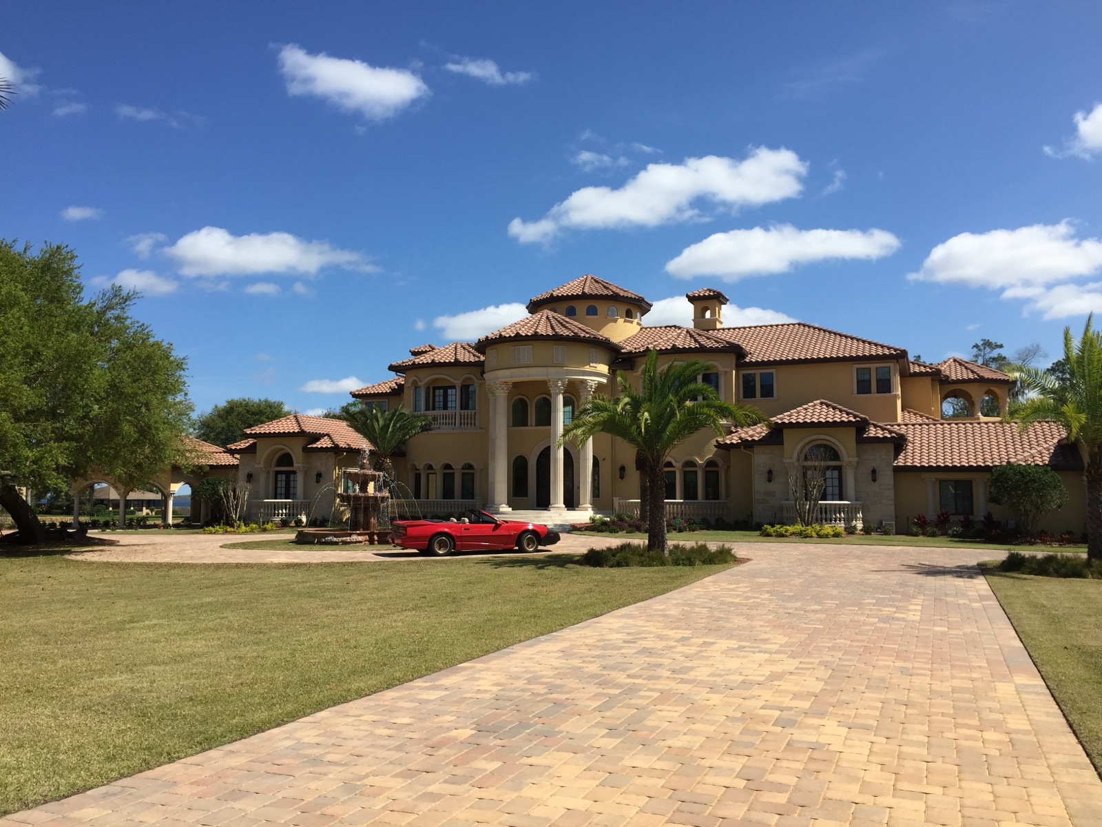 Brick paver driveway leading up to a large Florida home with palm trees