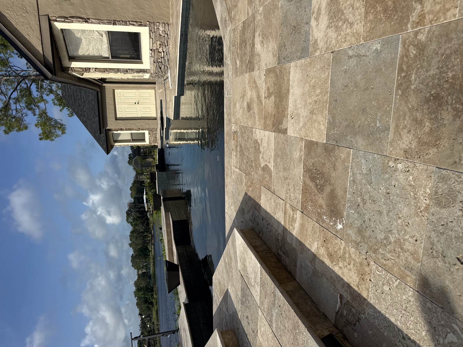 Travertine pool deck around a dark-tiled pool overlooking a lake