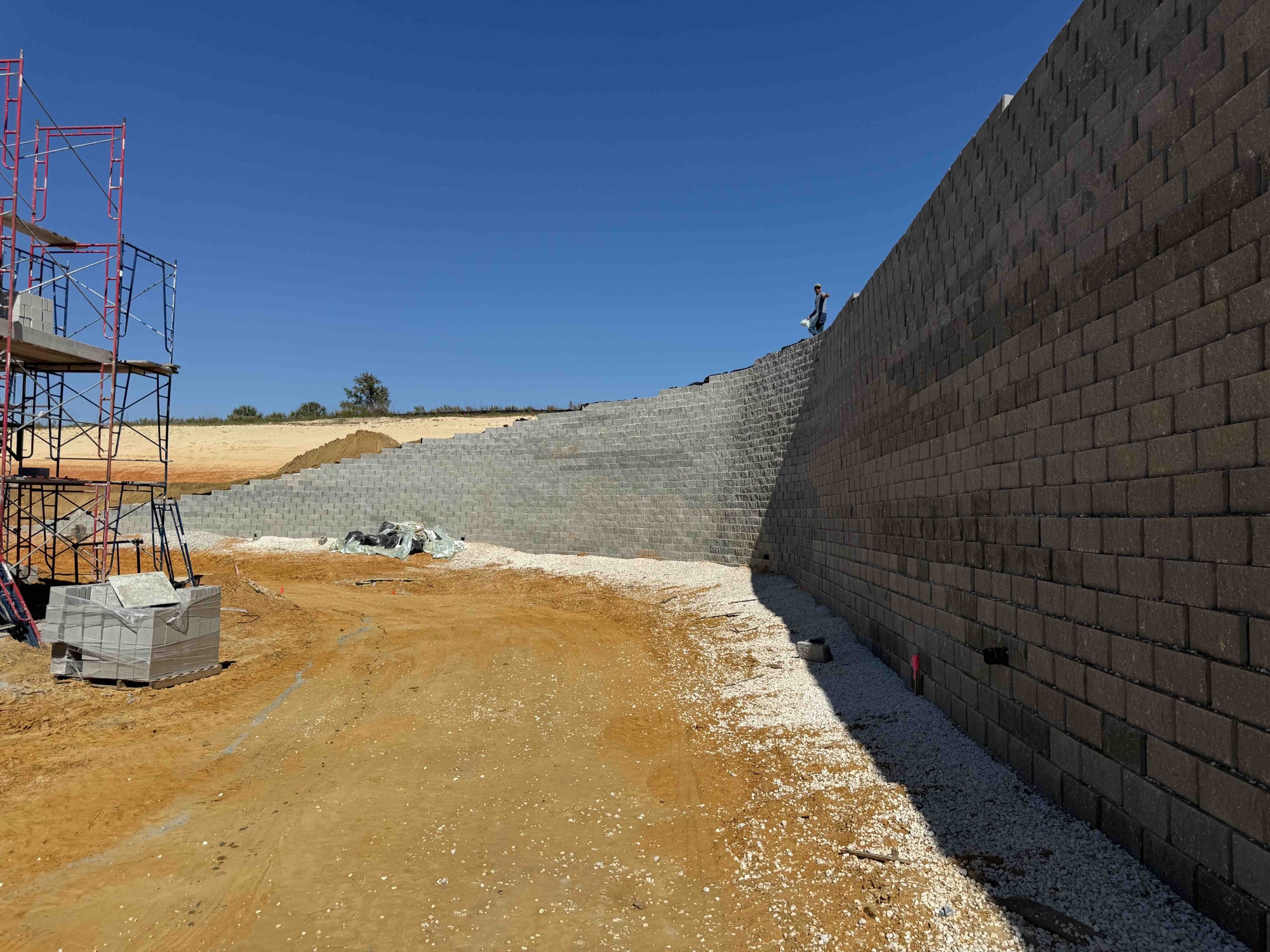 A tall segmental block retaining wall running along a graded site under a clear sky