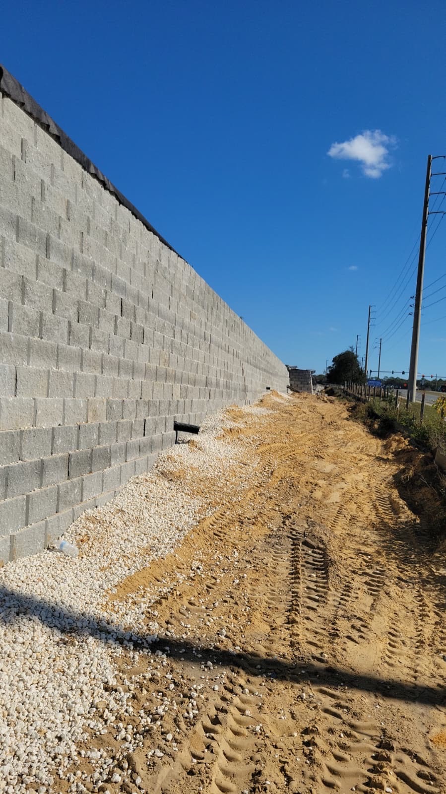 Finished segmental retaining wall along a roadside with stone backfill at its base